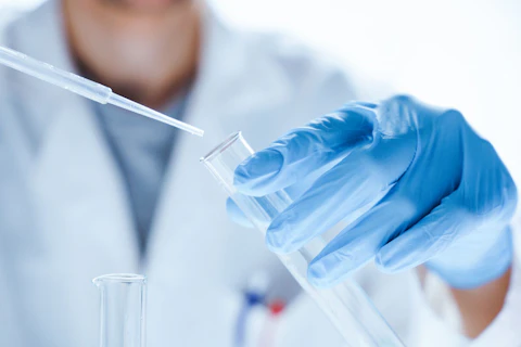 Pracownik laboratorium w rękawiczkach ochronnych przelewa badaną substancję do szklanej fiolki.